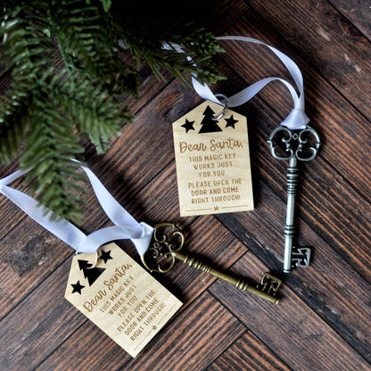 depicted are two beautiful bronze vintage skeleton keys tied with a white ribbon to a laser engraved christmas wooden letter to santa that says dear santa this magic key works just for you. please open the door and come right through